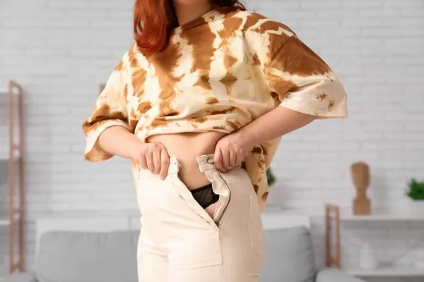 Image of woman trying to do her trousers up after pregnancy weight gain Skelmersdale